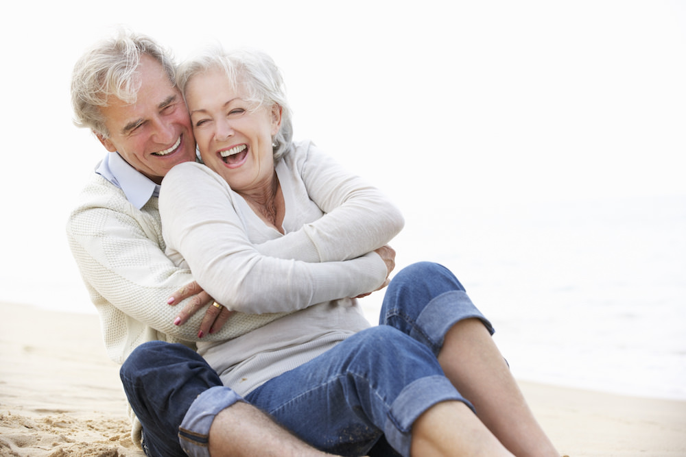 An elderly couple cuddling at the beach for vacation photo