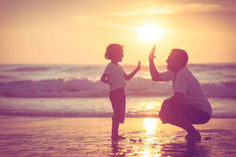 Dad and daughter high-fiving at the beach during sunset