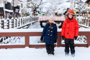 A boy and a girl posing in front of the bridge in snow looking warm