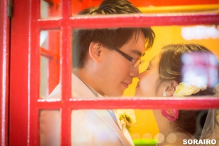 cA couple looking at each other romantically inside the telephone box with woman wearing wedding dress for pre-wedding photo