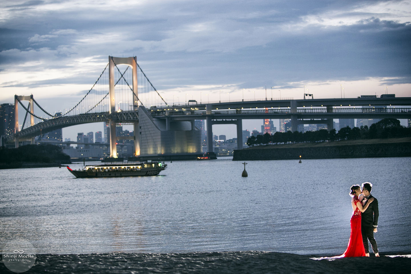 A couple kissing in Odaiba bay area during sunset with Tokyo tower and bridge in the background after sunset