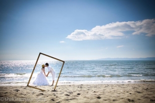 A couple kissing on the beach with woman wearing wedding dress as they fit into a frame for pre-wedding photo