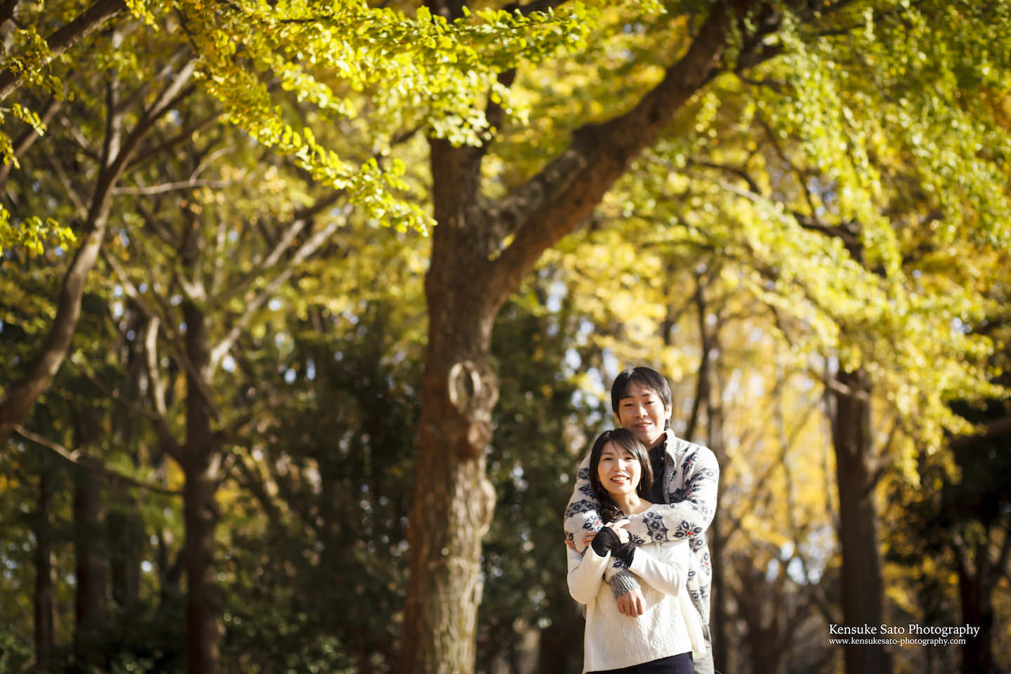A couple smiling in front of a camera in Yoyogi park in Autumn for pre-wedding photo