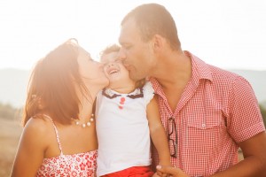 Happy family with mom and dad kissing their child during vacation photo