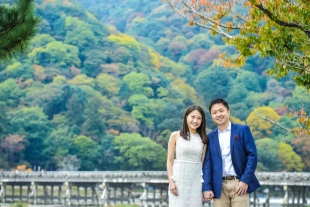 Vacation photo of a couple at Hozu river with Togetsukyo bridge in the background in Arashiyama, Kyoto