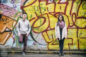 A couple smiling at the camera in front of a spray painted wall in Harajuku, Tokyo