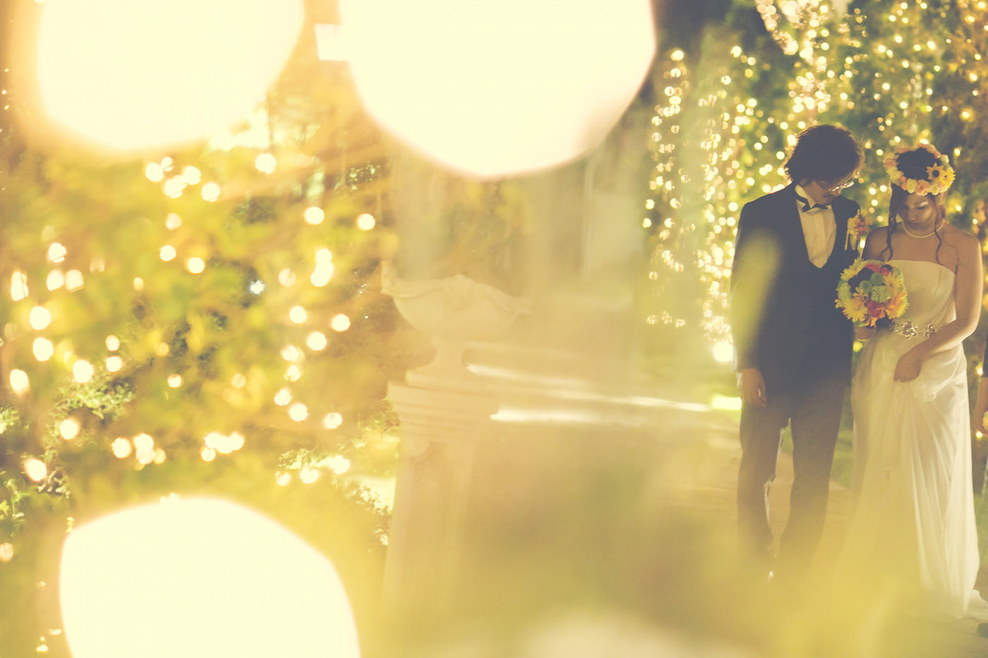 Pre-wedding photo by Ayako of a couple walking along lighted garden