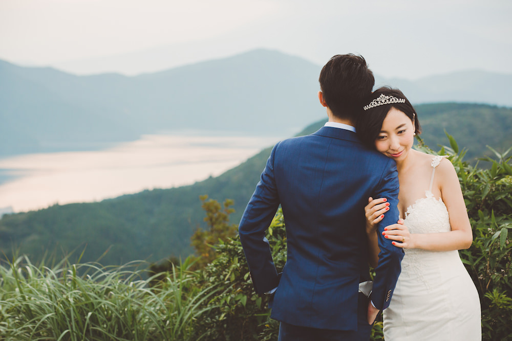 A woman holding on tight to her fiancé at Hakone mountain for pre-wedding photo with CHiKA